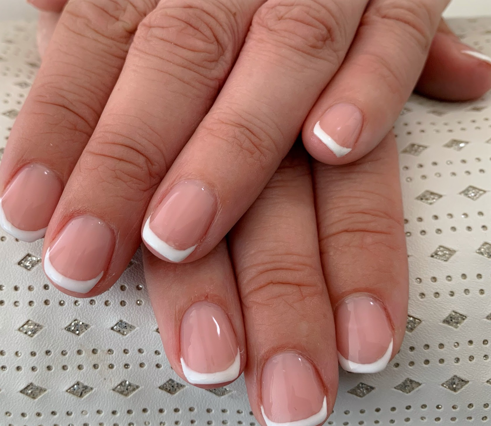 Gelakte vingernagels in roze met witte puntjes op een zilverkleurig doek
